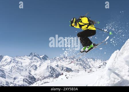 Un skieur en équipement sportif complet saute dans le précipice du sommet du glacier sur fond de ciel bleu et de neige caucasienne Banque D'Images