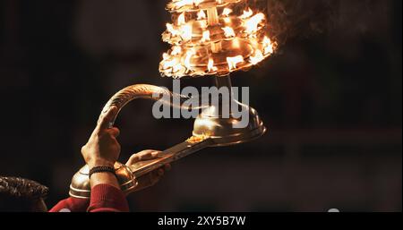 Varanasi, Inde. L'homme fait des mouvements avec un bougeoir avec des bougies allumées sur la cérémonie Ganga Maha Aarti commence. Brahman prêtre portant rouge et Banque D'Images