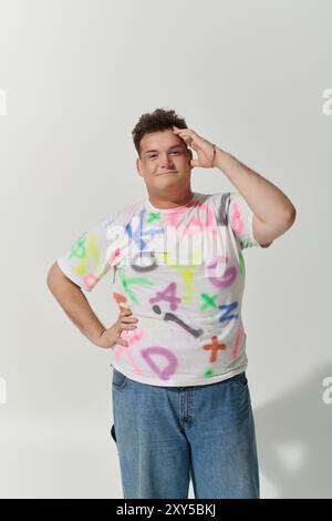 Jeune queer personne en t-shirt graffiti pose avec confiance sur fond blanc Banque D'Images