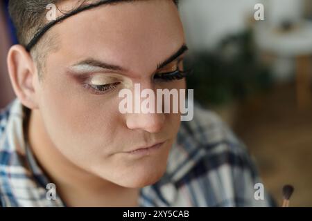 Une personne queer appliquant le maquillage avec une expression ciblée. Banque D'Images
