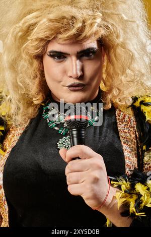 Une drag queen avec une grande perruque blonde et un maquillage accrocheur tient un microphone, prêt à chanter. Banque D'Images