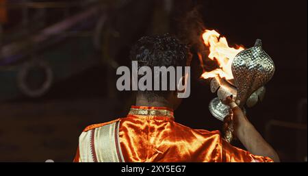 Varanasi, Inde. L'homme fait des mouvements avec un bougeoir avec des bougies allumées sur la cérémonie Ganga Maha Aarti commence. Brahman prêtre portant rouge et Banque D'Images