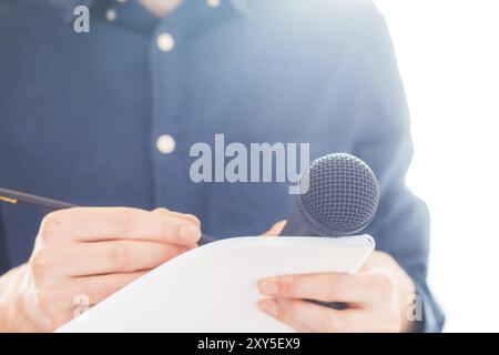 Cut-out d'un journaliste mâle dans un maillot bleu lors d'une conférence de presse qui est la prise de notes et la tenue d'un microphone Banque D'Images