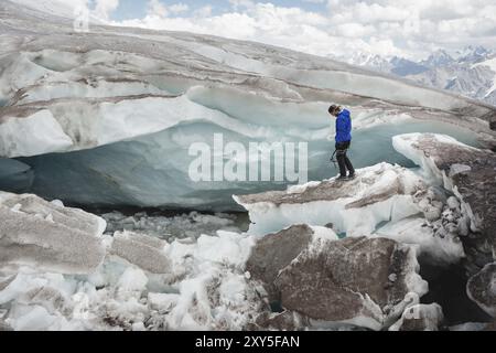 Le voyageur dans une casquette et des lunettes de soleil est assis dans les montagnes enneigées sur le glacier. Voyageur dans un environnement naturel Banque D'Images