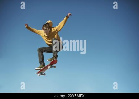 Un skateur adolescent fait un tour ollie dans un skatepark à la périphérie de la ville sur un fond de dégradé de ciel bleu Banque D'Images