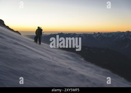 L'alpiniste professionnellement équipé à l'aube du soleil marche sur la pente au petit matin et la neige dérive sur la neige au-dessus de la neige. T Banque D'Images