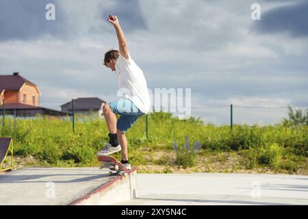 Garçon skateboarder dans un skate Park faisant un tour ollie sur un skateboard contre un ciel et des nuages d'orage Banque D'Images