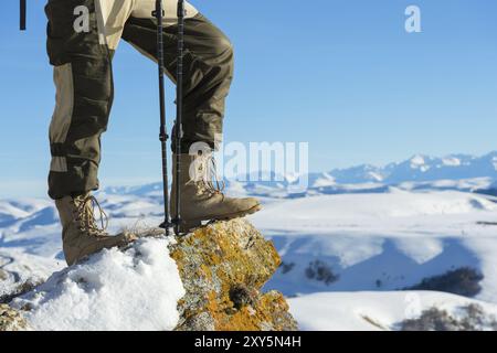 Gros plan du pied d'un touriste en bottes de trekking avec des bâtons pour la marche nordique debout sur une pierre dans les montagnes caucasiennes Banque D'Images