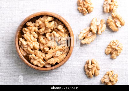 Demi-noyaux de noyer dans un bol en bois sur tissu de lin. Moitiés décortiquées et séchées de cerneaux de noix, graines mûres de noyer commun Juglans regia. Banque D'Images