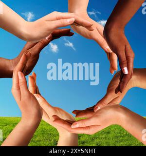 Symbole de paix conceptuelle et de diversité culturelle de mains multiraciales faisant un cercle ensemble sur fond de ciel bleu et d'herbe verte Banque D'Images