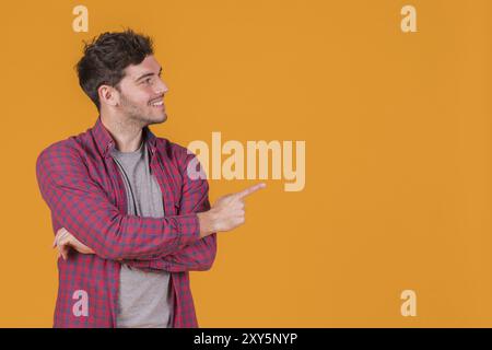 Portrait souriant jeune homme pointant son doigt sur fond orange Banque D'Images