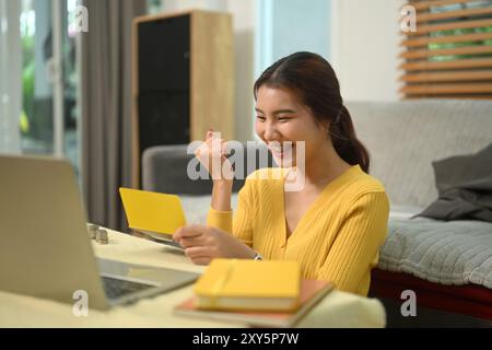 Jeune femme excitée regardant le livret de banque avec une expression heureuse, atteignant un jalon d'épargne Banque D'Images