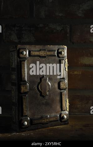 Gros plan de livre ancien rustique avec couverture en cuir ornemental dur illuminé dans l'obscurité artistique nature morte dramatique Banque D'Images