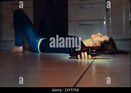 Jeune femme allongée sur le sol de la cuisine avec une bouteille de bière Banque D'Images