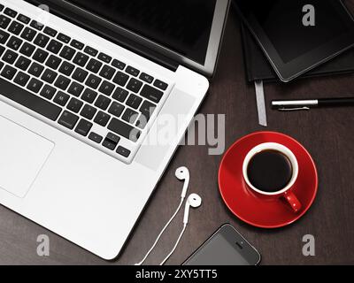 Ordinateur portable Apple Macbook, iPhone avec écouteurs, tablette Kindle Fire et une tasse de café rouge sur un bureau still life Banque D'Images