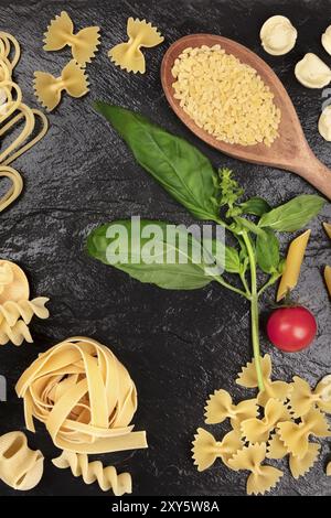 Une photo prise à la verticale de différents types de pâtes au basilic et tomates cerises, tourné à partir de ci-dessus, sur un fond noir, formant une trame pour copy space Banque D'Images