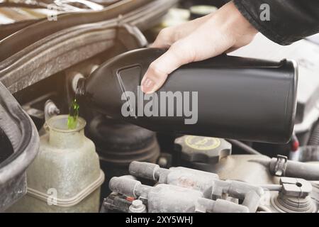 La jeune fille ajoute le niveau du liquide de refroidissement dans le moteur de sa voiture sur la route à un voyage à la campagne. Le concept d'inspection technique opportune de la voiture Banque D'Images