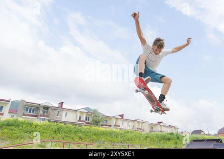 Jeune skateboarder intense en saut en hauteur contre le ciel et les zones de couchage Banque D'Images