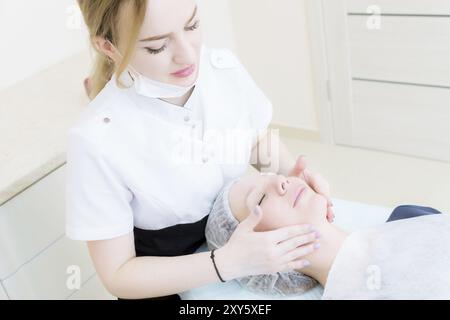 Salon de beauté. Gros plan d'une esthéticienne médicale dans des gants roses fait un massage du visage d'une belle femme. Cosmétologie. Tête et épaules d'une fille wi Banque D'Images