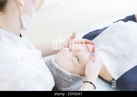 Salon de beauté. Gros plan d'une esthéticienne médicale dans des gants roses fait un massage du visage d'une belle femme. Cosmétologie. Tête et épaules d'une fille wi Banque D'Images