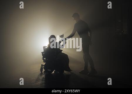 Femme handicapée recevant une coupe de victoire alors qu'elle était assise dans un fauteuil roulant dans une pièce sombre avec un rétroéclairage blanc. Banque D'Images