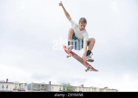 Jeune skateboarder intense en saut en hauteur contre le ciel et les zones de couchage Banque D'Images