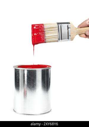 Gros plan d'une main de personne tenant un pinceau trempé dans une boîte avec de la peinture rouge isolé sur fond blanc. Rénovations et concept de peinture Banque D'Images