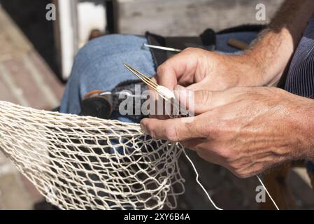 Enkhuizen, pays-Bas. Juin 2022. Les mains d'un pêcheur réparant les filets de pêche avec aiguille et fil. Gros plan Banque D'Images