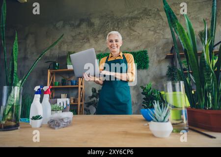 Photo de Shiny Happy Age femme habillée tablier rassemblant des plantes texto gadget à l'intérieur atelier à la maison Banque D'Images