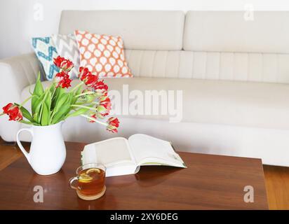 Beau bouquet de tulipes orange avec un plateau et le livre sur la table en bois dans le salon Banque D'Images