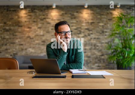 Entrepreneur contemplatif avec la main sur le menton regardant loin tout en travaillant sur ordinateur portable au bureau dans le bureau Banque D'Images