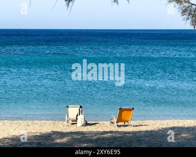 Plage tropicale avec deux chaises longues vides, océan de mer ondulé et fond de ciel bleu. Détente des vacances d'été. Banque D'Images