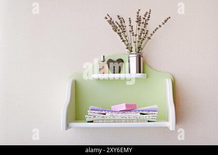 Savon rose, textile placé sur une étagère verte décorée de fleur en pierre en forme de coeur sur mur blanc dans une chambre confortable moderne. Concept de nettoyage de printemps Banque D'Images