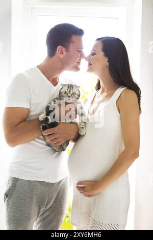 Jeune homme avec la jolie femme enceinte et cat indoors Banque D'Images