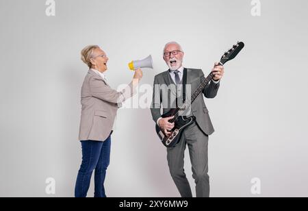 Femme d'affaires senior chantant par mégaphone et homme d'affaires jouant de la guitare sur fond blanc Banque D'Images