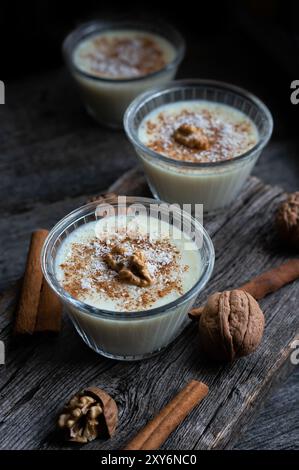 Pudding dans un bol en verre avec cannelle et noix sur une table rustique, dessert au lait Banque D'Images