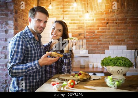 Jeune couple souriant mangeant de la pizza maison ensemble à la cuisine Banque D'Images