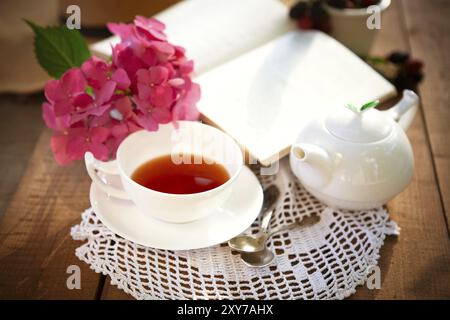 Du dessus de la tasse de thé rouge et de thé blanc en céramique sur table en bois avec des fleurs roses et livre ouvert Banque D'Images