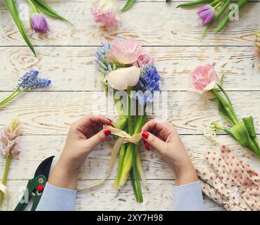 Un fleuriste au travail. Femme faisant bouquet de fleurs de printemps sur la table en bois rustique Banque D'Images