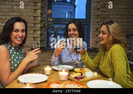 Trois femmes friends toasting with red wine dans la cuisine. L'accent sur la femme moyenne Banque D'Images