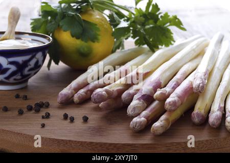 Asperges pelées et ingrédients pour une sauce sur planche de bois Banque D'Images