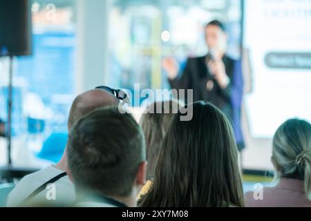 Auditoire écoutant attentivement un orateur qui présente lors d'un événement professionnel. Arrière-plan flou avec accent sur les participants. Banque D'Images