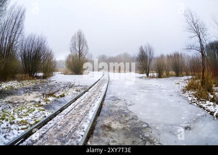 Pont routier en bois à travers le lac gelé dans la journée brumeuse Banque D'Images