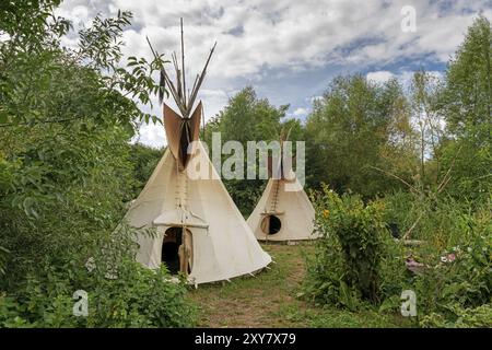 Deux tipis indiens se tiennent au soleil dans une prairie entre les arbres et les buissons Banque D'Images