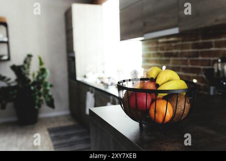 Fruits tropicaux : noix de coco cassée, pomme, mandarine, orange, banane dans un bol de fruits sur le comptoir de bar dans une cuisine loft élégante. Arrière-plan flou. Banque D'Images