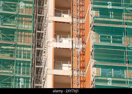 Gros plan d'un chantier de construction avec échafaudage et filet de sécurité vert, présentant un immeuble de grande hauteur non fini avec béton et briques apparents Banque D'Images