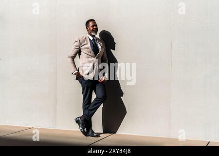 Homme d'affaires noir mature portant costume élégant se promenant dans la ville - homme senior adulte africain corporatif avec barbe grise sur le mur industriel Banque D'Images