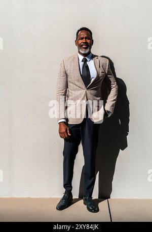 Homme d'affaires noir mature portant costume élégant se promenant dans la ville - homme senior adulte africain corporatif avec barbe grise sur le mur industriel Banque D'Images