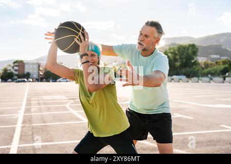 Beau couple senior heureux jouant au basket-ball et s'amusant - couple marié mature dans l'amour se lier à l'extérieur et faire du sport ensemble, concepts ab Banque D'Images