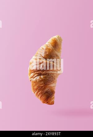 Croissant fraîchement cuit, levant ou volant. Un croissant vole dans l'air isolé sur fond rose. Scène de lévitation. Copier un espace pour le texte. Signature Banque D'Images